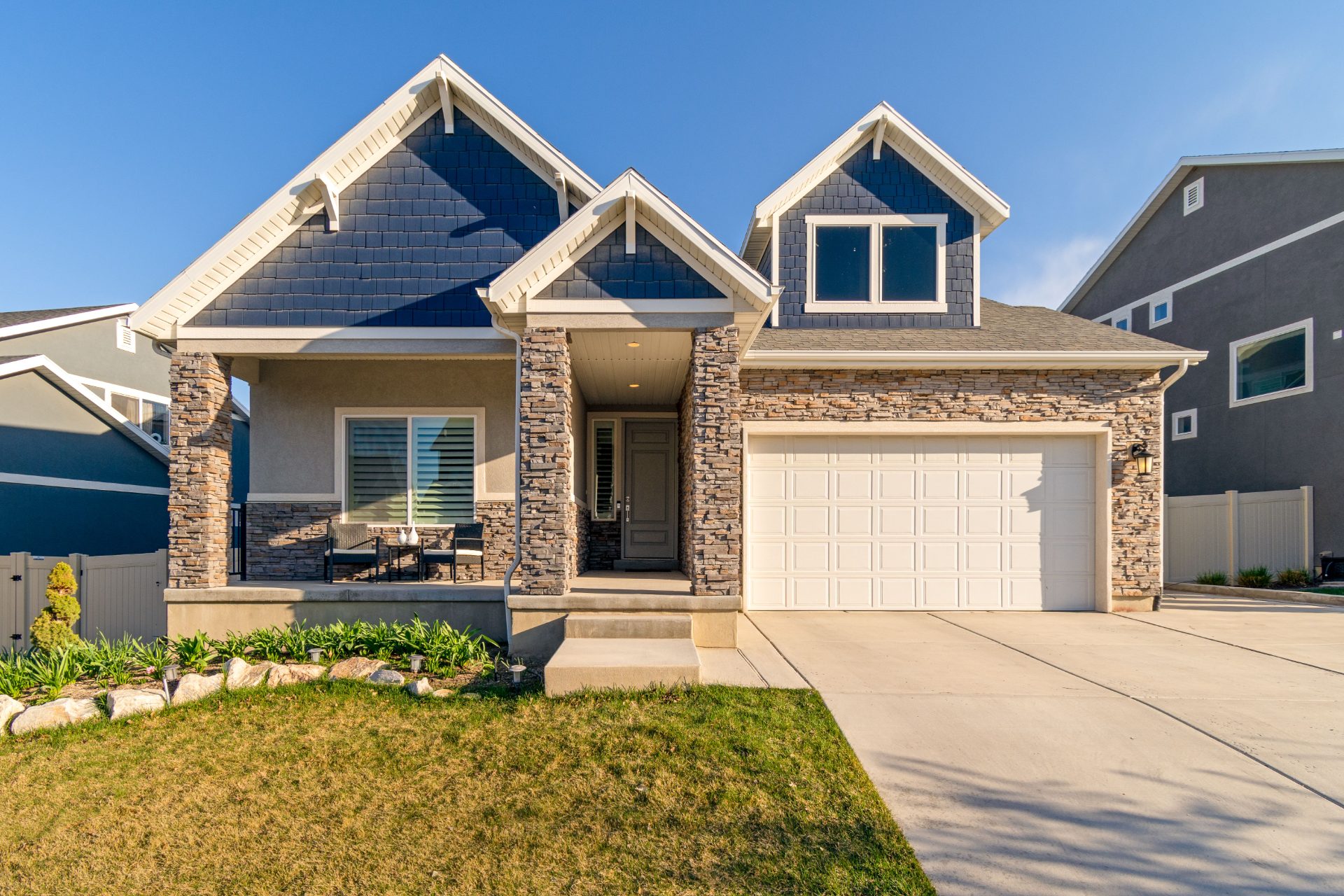Craftsman-style home with stone columns, a covered front porch, and a two-car garage