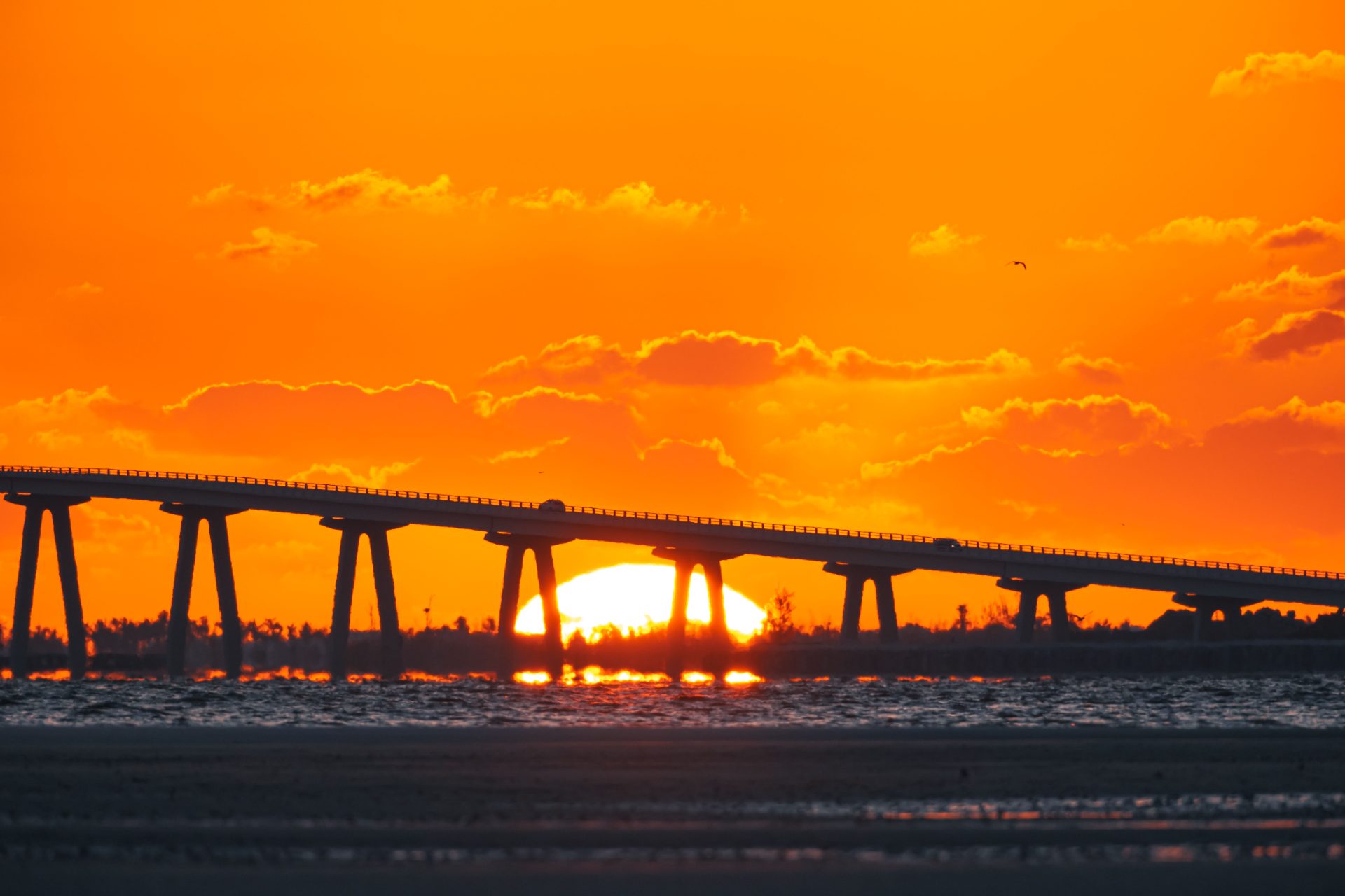 Sun setting behind a long causeway bridge over the water