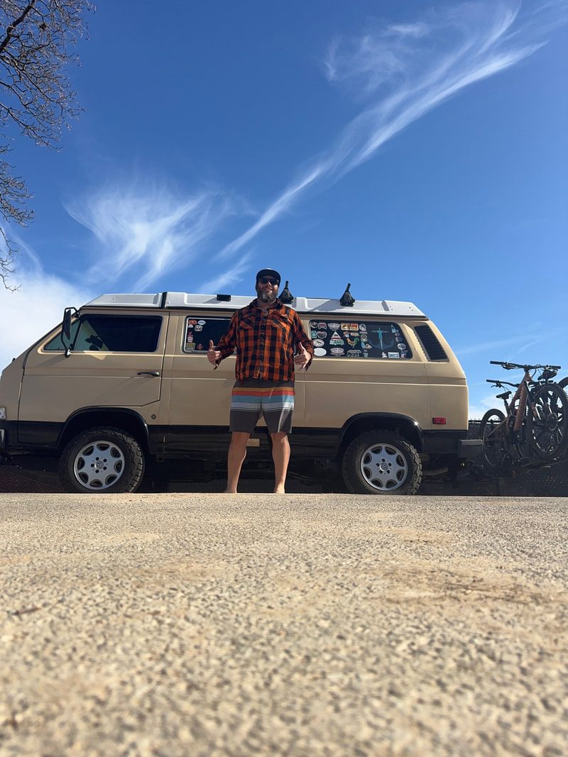 Dan Saffer standing in front of his tan camper van on a sunny day, giving two thumbs up