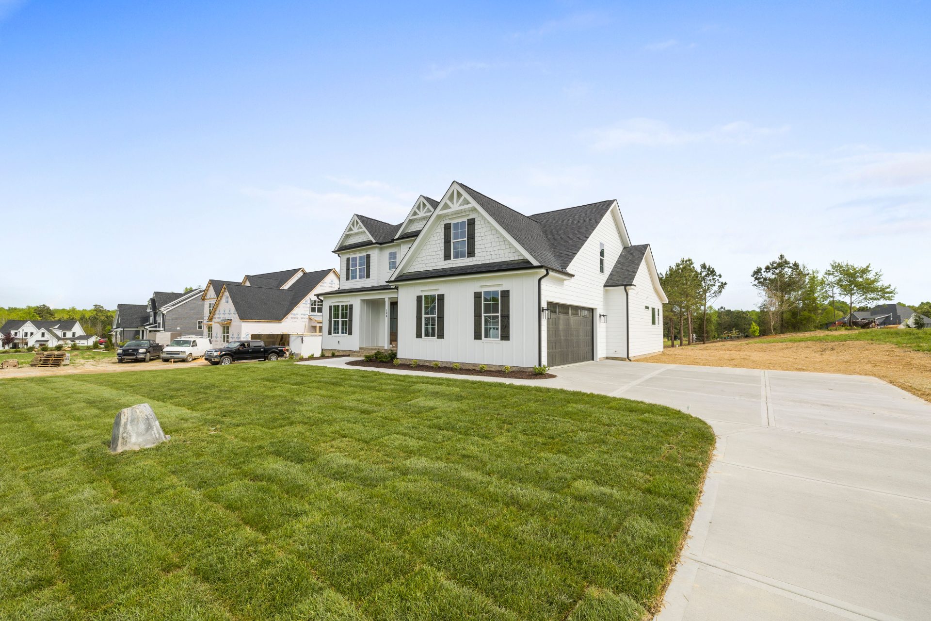 New white two-story home with a fresh lawn, with more homes under construction behind it
