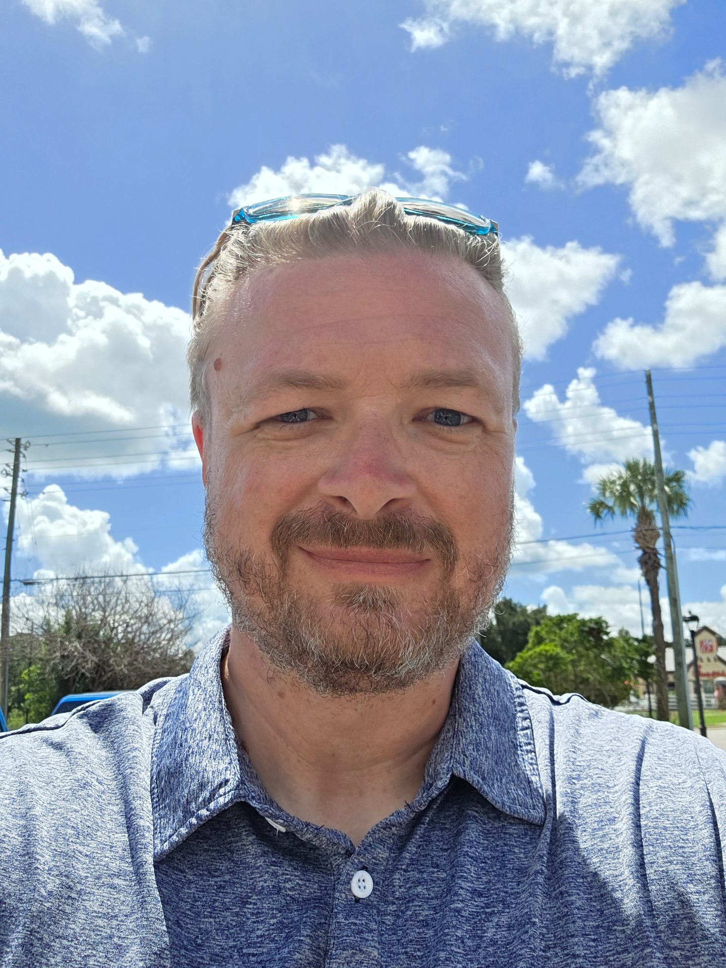 George VanLare smiling outdoors on a sunny day, palm tree and blue sky behind him