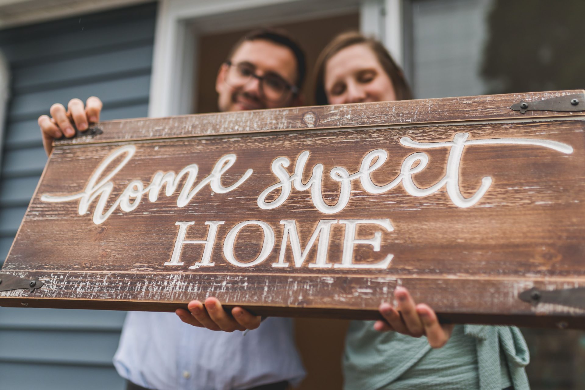 Couple on their front step holding a Home Sweet Home sign