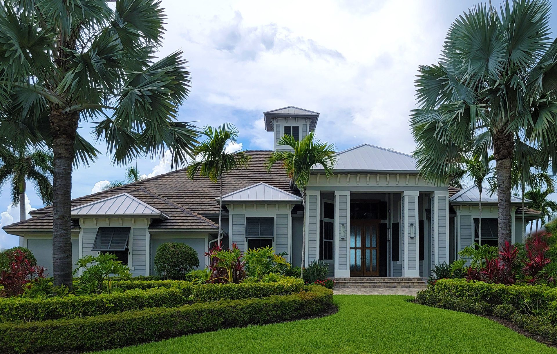 Single-story home with a metal roof and cupola, framed by palms and tropical landscaping