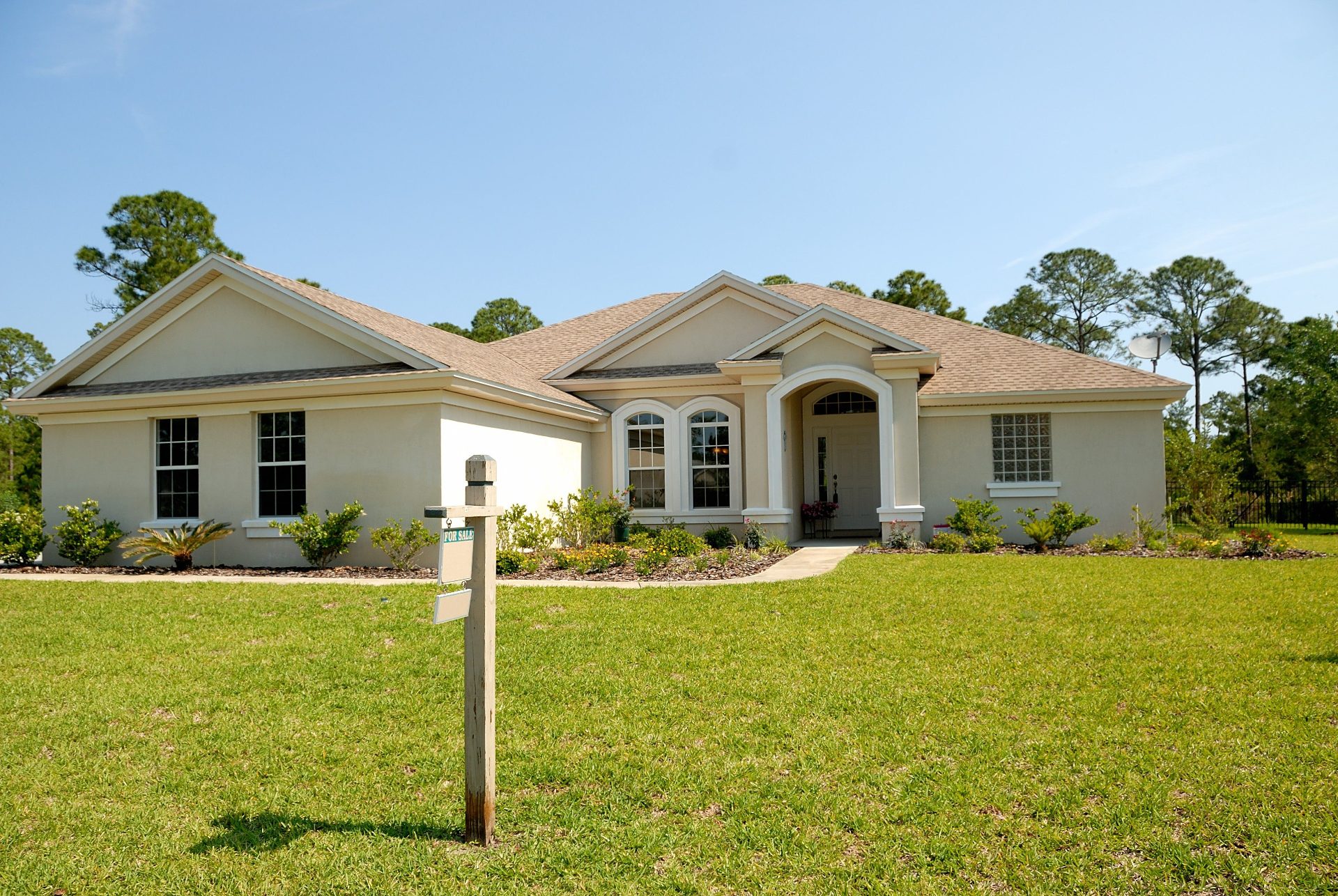 Single-story stucco home with a For Sale sign on the front lawn